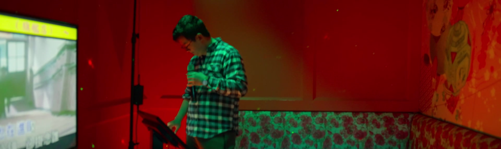 A singer performing under red karaoke-room lights